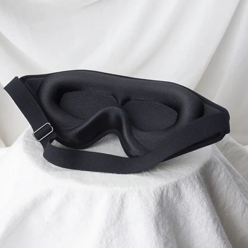 Contoured memory-foam blackout sleep mask resting on white fabric